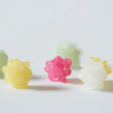 Small, textured, flower-like candies in pastel colors, including pink, yellow, white, and light green, arranged on a plain white surface with a shallow depth of field.