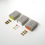 Three small Konfeidou boxes arranged on a white background with scattered decorative flower-shaped candies beside them.