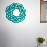A Sailor's Wreath in varying shades of blue and green made from lobster rope hanging on a white wall with mirror
