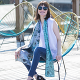 A woman wearing sunglasses and a sleeveless white top, accessorized with a two-sided silk scarf featuring blue and white patterns.