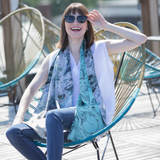 A woman wearing sunglasses and a sleeveless white top, accessorized with a two-sided silk scarf featuring blue and white patterns.