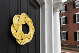 A handcrafted yellow rope sailor's wreath with a traditional Turk’s Head knot, hanging on a dark door.
