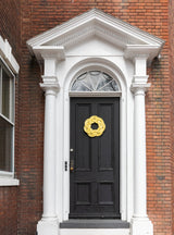 A handcrafted yellow rope sailor's wreath with a traditional Turk’s Head knot, hanging on a dark door.