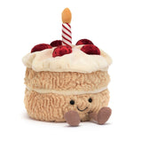 A plush toy in the shape of a birthday cake with two layers, decorated with a red and white striped candle on top and a smiley face on the front.