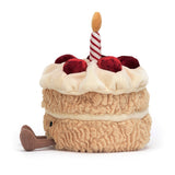 A plush toy in the shape of a birthday cake with two layers, decorated with a red and white striped candle on top and a smiley face on the front.