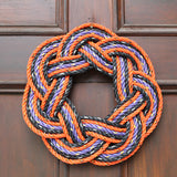 A Sailor's wreath made from lobster rope in orange, black and purple colours on a dark brown door.