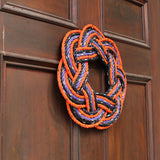 A Sailor's wreath made from lobster rope in orange, black and purple colours on a dark brown door.