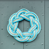 A handcrafted sailor's wreath made of rope, with colors resembling sand, sea, and sky, displayed on a door.