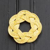 A handcrafted yellow rope sailor's wreath with a traditional Turk’s Head knot, hanging on a dark door.