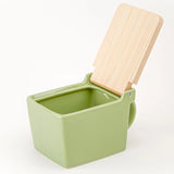 A square ceramic salt box in sage green with a hinged wooden lid, shown on a clean white background.