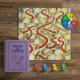 Vintage Chutes and Ladders game set on a wooden surface with a purple book titled 'Chutes and Ladders'.