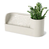 A modern tabletop fountain and planter combo in a warm beige finish, featuring a cylindrical planter with a green artificial plant and a ribbed waterfall panel on a white background.