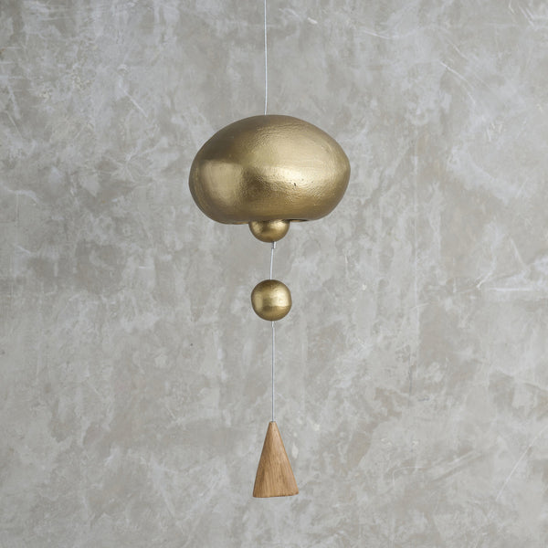 Brass and wooden hanging bell against a gray concrete wall