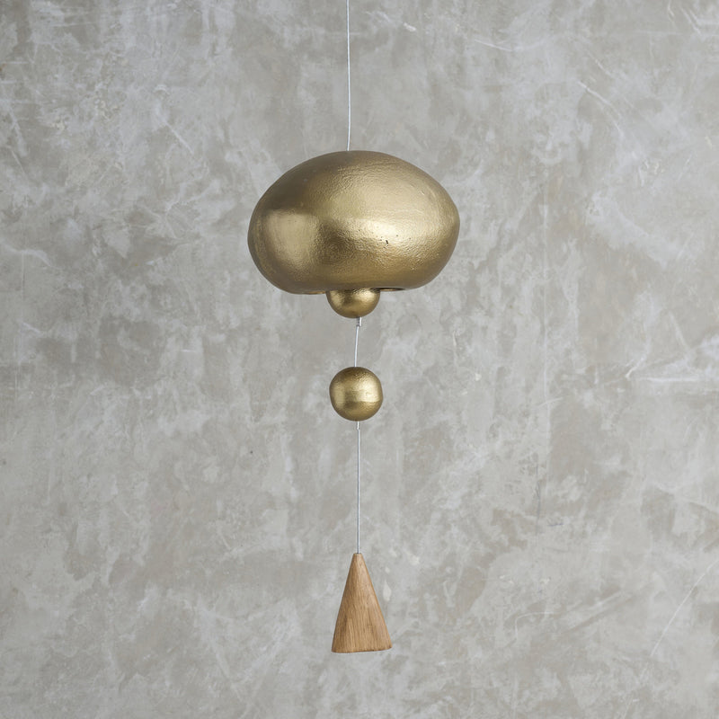Brass and wooden hanging bell against a gray concrete wall