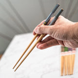Hand holding a pair of wooden chopsticks with a blurred background