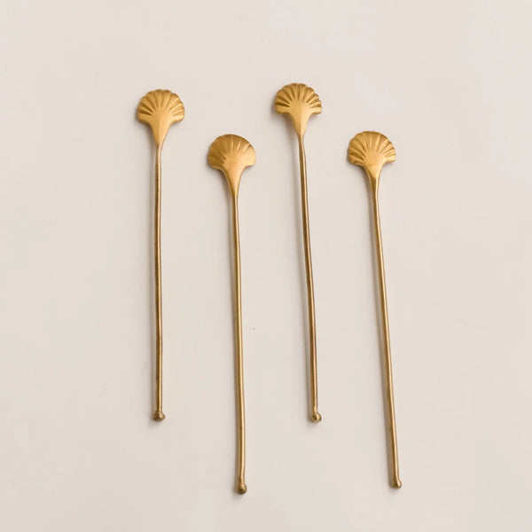 Four gold shell-shaped stir sticks on a beige background