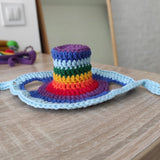 Colorful crocheted cat hat in rainbow colours on a neutral surface.