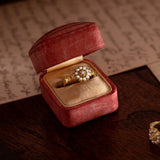 Gold ring in a red velvet box on a wooden surface with an envelope and sealing wax.