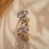 Four ornate rings with pearls and gemstones on a beige fabric background