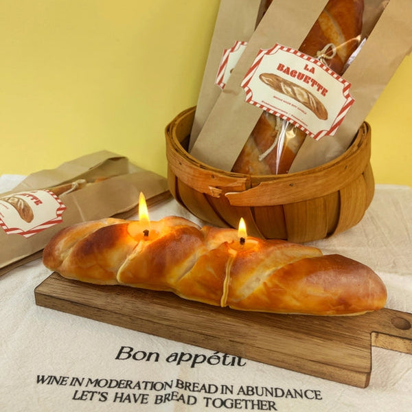 Bread-shaped candles on a wooden board with a basket of bread in the background.