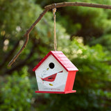 Red and white birdhouse hanging from a branch with a blurred green foliage background