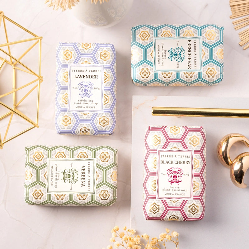 Four soap bars with decorative packaging on a light surface.