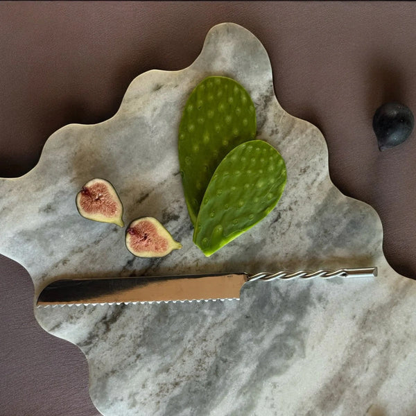 Marble cutting serving board with figs and a cactus leaf on a brown background
