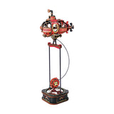 A decorative steampunk-style mechanical sculpture featuring a red and black submarine-like machine mounted on a tall stand with a circular base, photographed on a plain white background.