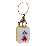 A miniature Mahjong keychain featuring a white tile with red and blue Chinese characters, attached to a gold-tone metal key ring and clasp, shown on a plain white background.