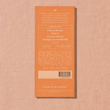 The back of an orange Spring & Mulberry brand product box, showing ingredients, nutrition facts, and a barcode, set against a textured pink background.