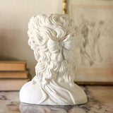 White marble bust of a classical figure on a marble surface with books and a painting in the background.
