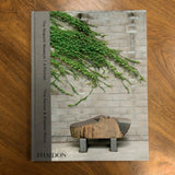 A hardcover book titled 'The Nagoldi Museum | A Portrait' by Tina Barny & Stephen Shore, published by Phaidon, lying flat on a wooden surface. The cover features a photograph of green ivy climbing a gray brick wall with a stone bench in the foreground.