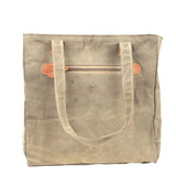 A canvas tote bag in a muted taupe-beige color with light brown leather accents on the zipper pull and strap attachments, shown against a plain white background.