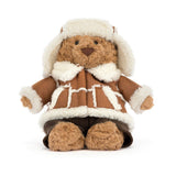 A plush teddy bear wearing a brown and cream faux-fur winter outfit with a matching hat, photographed on a clean white background.