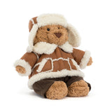 A plush teddy bear wearing a brown and cream winter coat with a matching cream fur-trimmed hat, seated against a plain white background.