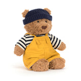 Teddy bear wearing a navy hat, striped shirt, and yellow overalls on a white background
