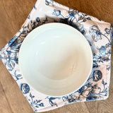 White bowl on a floral-patterned cozy plate on a wooden surface