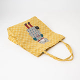 A yellow reusable tote bag with a repeating polka dot pattern and a whimsical cat on the front, shown on a clean white background.