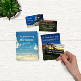Set of cards with affirmations on a white surface with a plant in the corner