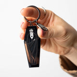 Hand holding a black coffin-shaped keychain with an bat design on a white background