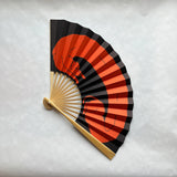 A traditional folding hand fan with a black and orange dog print displayed on a textured light gray background.