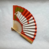 Decorative fan with red, gold, and white design on a light gray background