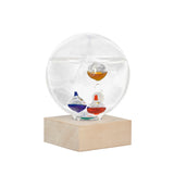 Kikkerland Galileo Thermometer, featuring a 4-inch glass sphere with colored liquid thermometers inside, resting on a wooden base.