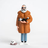 Figurine of Edward Gorey in a brown coat holding a black and white cat on a white background