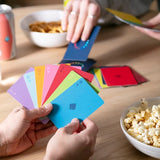 Colorful card game being played on a wooden table with snacks and drinks.