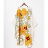 A cream-colored kimono-style wrap with a large yellow floral print, hanging on a wooden hanger against a white paneled wall.