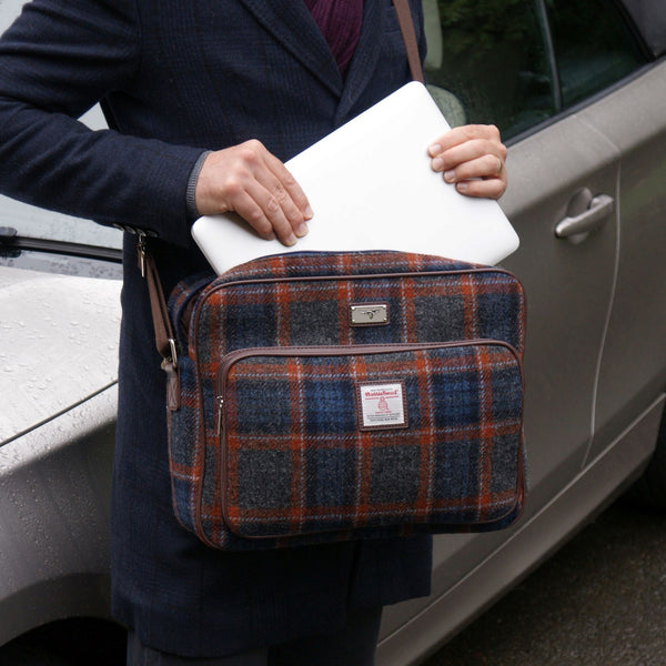 Person holding a plaid bag and white laptop next to a car