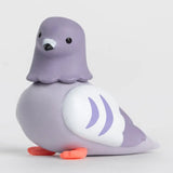 A cute, stylized toy pigeon figurine in shades of lavender purple, white, and bright orange feet, set against a clean light gray background.