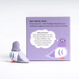 A cute, stylized toy pigeon figurine in shades of lavender purple, white, and bright orange feet, set against a clean light gray background.