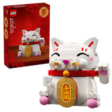 LEGO brick building set box and assembled Lucky Cat toy on a white background. The red retail box shows the LEGO branding and product details, while the assembled toy in front is mostly white with a red collar, gold coin detail, pink paws/ears, and black closed-eye expression.